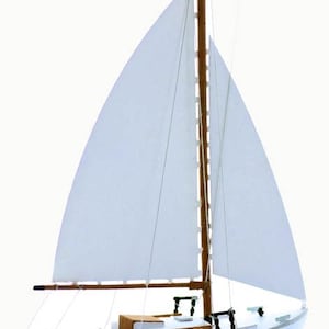 May include: A white wooden sailboat model with a brown mast and white sails. The boat has a small cabin and a wooden deck.