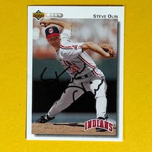 May include: A baseball card featuring Steve Olin in a pitching pose. He is wearing a Cleveland Indians uniform with the team logo on his cap. The card has the Upper Deck logo and a signature.
