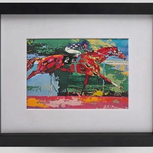 May include: A framed art print featuring an impressionistic painting of two racehorses in motion with jockeys. The horses are rendered in vibrant red and orange tones against a green and blue background. A black frame surrounds the white matting.