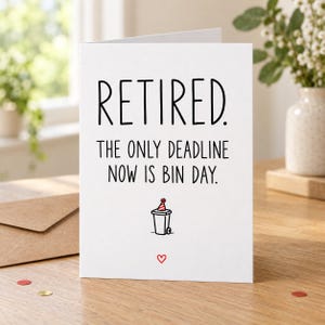 Lifestyle mock-up of a standing card reading “RETIRED. THE ONLY DEADLINE NOW IS BIN DAY.” with a wheelie bin in a party hat. On a wooden table beside a Kraft envelope and red/gold confetti.