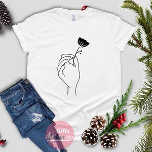 May include: White t-shirt with a black line drawing of a hand holding a flower.