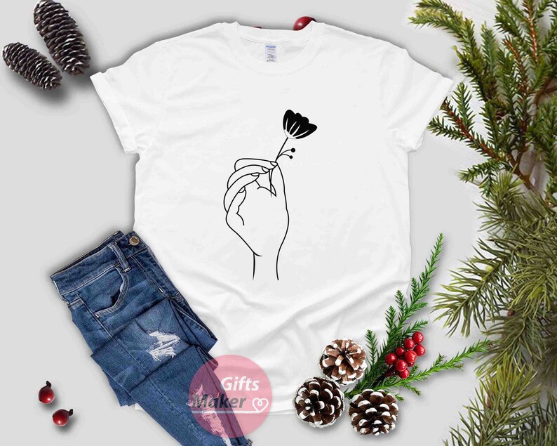 May include: White t-shirt with a black line drawing of a hand holding a flower.