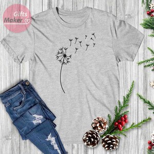 May include: A gray t-shirt with a black dandelion graphic. The dandelion is blowing in the wind and has seeds flying off of it.