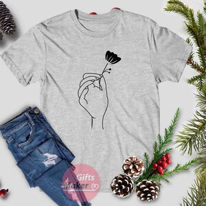 May include: A gray t-shirt with a black line drawing of a hand holding a flower.