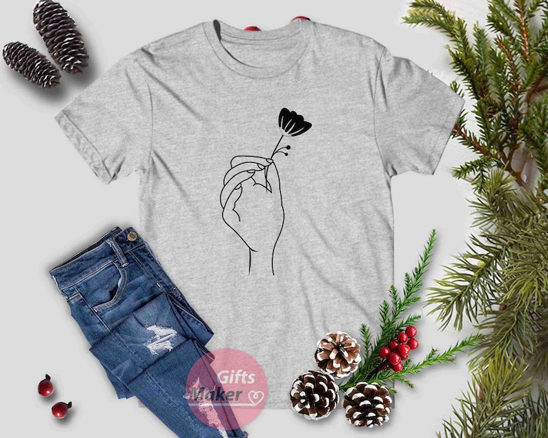 May include: A gray t-shirt with a black line drawing of a hand holding a flower.