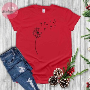 May include: A red t-shirt with a black dandelion graphic. The dandelion has seeds blowing in the wind.