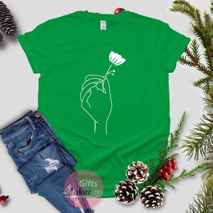 May include: A green t-shirt with a white outline of a hand holding a flower.