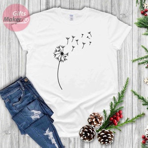 May include: White t-shirt with a black dandelion graphic. The dandelion has seeds blowing in the wind.