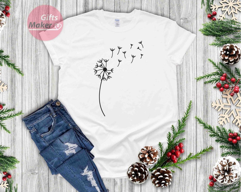 May include: White t-shirt with a black dandelion graphic. The dandelion has seeds blowing in the wind.
