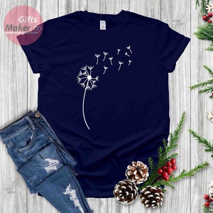 May include: A navy blue t-shirt with a white dandelion graphic. The dandelion has seeds blowing in the wind.