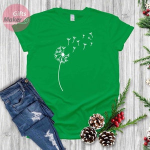May include: A green t-shirt with a white dandelion graphic. The dandelion has seeds blowing in the wind.