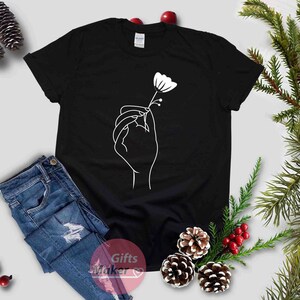 May include: Black t-shirt with a white line drawing of a hand holding a flower.