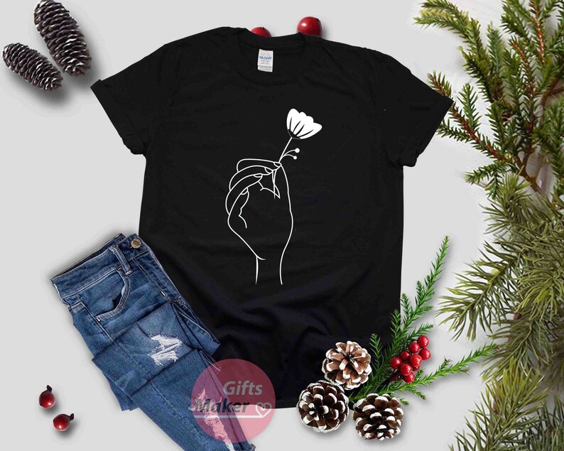 May include: Black t-shirt with a white line drawing of a hand holding a flower.