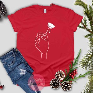 May include: A red t-shirt with a white outline of a hand holding a flower.