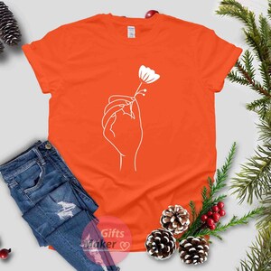 May include: Orange t-shirt with a white outline of a hand holding a flower.