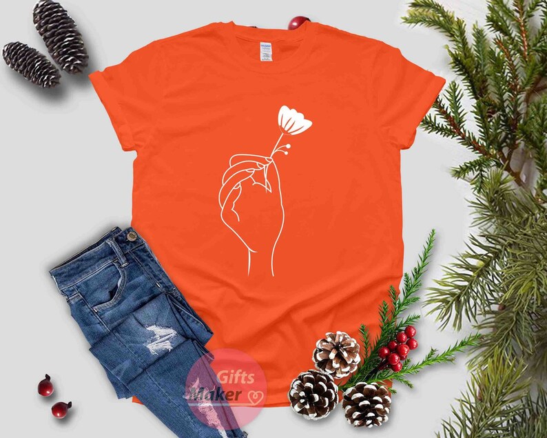 May include: Orange t-shirt with a white outline of a hand holding a flower.