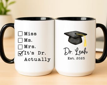 May include: White ceramic mug with a black handle and rim. One side features a checklist with "It's Dr. Actually" checked. The other side displays a graduation cap graphic, the name "Dr. Leah", and "Est. 2025".
