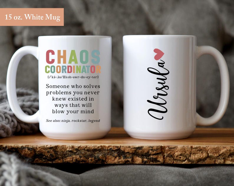 May include: Two white ceramic mugs. One mug has the text "Chaos Coordinator" with a definition and the text "See also: ninja, rockstar, legend". The other mug has the text "Ursula" with a red heart above the name.