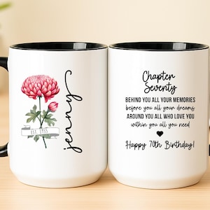 May include: White ceramic mug with a black handle and rim. One side features a pink flower and the name "Jenny". The other side has the text "Chapter Seventy" and a birthday message. A personalized gift.
