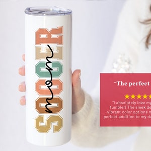May include: White tumbler with the word "Soccer" in colorful retro-style letters and the word "Mom" written in cursive. The tumbler is being held by a hand. The text "The perfect gift" is written in red with five yellow stars below it.