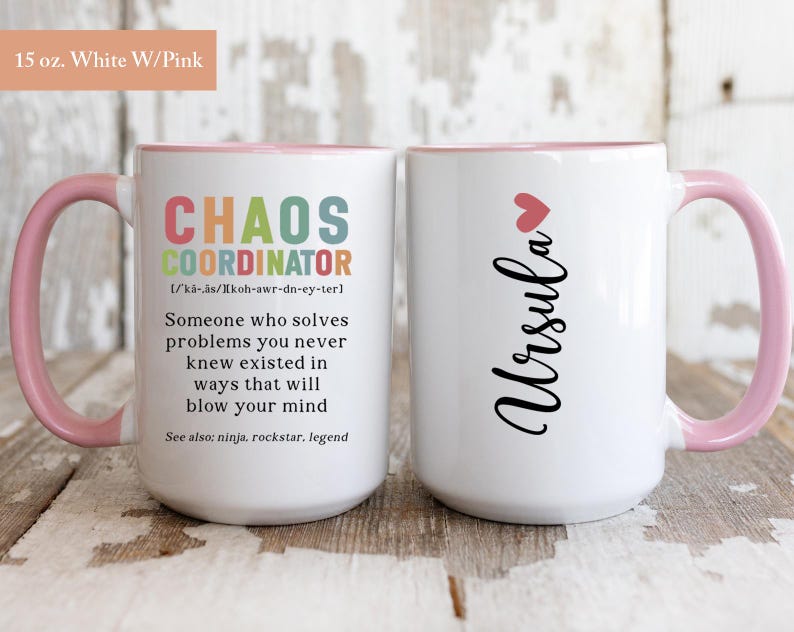 May include: White ceramic mug with a pink rim and handle. The mug features a black design that reads "Chaos Coordinator" with a definition and the name "Ursula" on the other side.