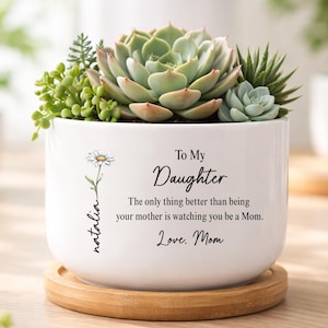 May include: A white ceramic planter with a wooden base, filled with succulents. The planter has a daisy graphic and text that reads "To My Daughter...Love, Mom" with the name "natalia" on the side. The succulents are green and beige.