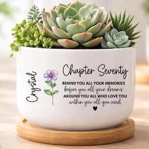 May include: White ceramic planter with a wooden base, filled with succulents and small plants. The planter has the name "Crystal" and the words "Chapter Seventy" with a floral design. Text includes "BEHIND YOU ALL YOUR MEMORIES before you all your dreams AROUND YOU ALL WHO LOVE YOU within you all you need."
