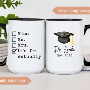 May include: White ceramic mug with a black handle and rim. One side reads "It's Dr. Actually" with check boxes. The other side features a graduation cap graphic and the text "Dr. Leah Est. 2025".