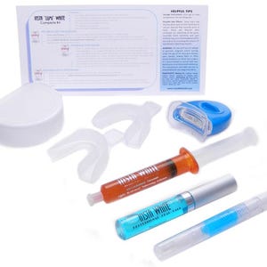 Peut inclure: Un kit complet de blanchiment des dents avec le texte "Insta Lumi White". Le kit comprend un étui blanc, des gouttières, des seringues avec du gel orange et bleu, une lumière LED bleue et une notice.