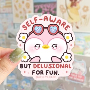 Puede incluir: Un ping&uuml;ino rosa con gafas en forma de coraz&oacute;n con el texto "SELF-AWARE BUT DELUSIONAL FOR FUN." y el nombre de usuario de las redes sociales "@GELLYROISE".