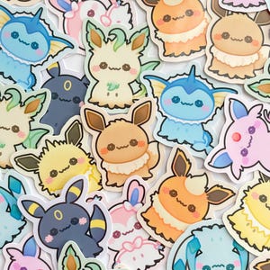 May include: A collection of colorful, die-cut stickers featuring various cartoon creatures with large eyes and cute expressions. The stickers are in shades of blue, pink, yellow, orange, and black, with white outlines.