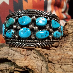 May include: A silver bracelet with turquoise stones set in a silver band. The bracelet has a braided design on the band.