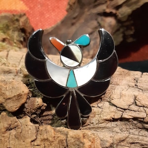 Puede incluir: Un colgante de pájaro negro y blanco con acentos turquesa y rojos. El pájaro está hecho de plata y tiene un diseño detallado.