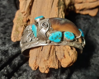 May include: A silver bracelet with turquoise stones and a bear claw charm. The bracelet is decorated with intricate silverwork.