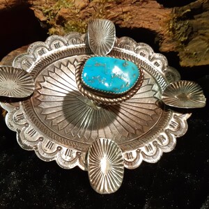 Puede incluir: Una hebilla de cinturón de estilo nativo americano en plata y turquesa con un diseño detallado. La hebilla es de forma ovalada y tiene una piedra turquesa en el centro.