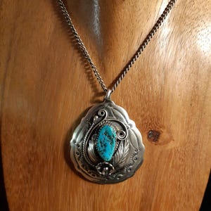 Può includere: Una collana con ciondolo in argento caratterizzata da una pietra turchese ovale con motivi a matrice scura. La montatura in argento è decorata con dettagli stampati complessi, motivi a foglia e volute. Il ciondolo pende da una sottile catena.