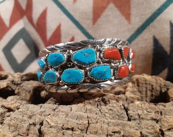 May include: A silver bracelet with turquoise and coral stones. The bracelet has a braided design and is set with multiple stones.