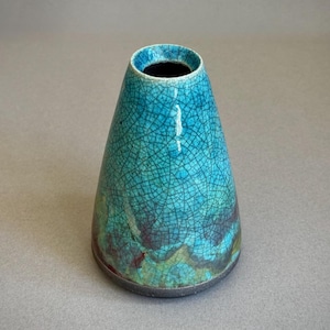 Peut inclure: Un vase en céramique de forme conique arborant un émail turquoise vif avec un motif craquelé sombre prononcé. La surface présente des dégradés subtils de vert et de brun foncé près de la base, finie par un bord sombre, texturé et non émaillé.