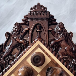 May include: A wooden chessboard with intricate carvings of lions and a crown. The board is made of dark wood with a light wood inlay. The chess pieces are not included.