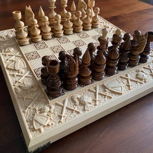 May include: A wooden chess set with intricately carved pieces and a board with a decorative border. The pieces are arranged on the board in a starting position. The board is made of light wood and has a dark wood inlay. The pieces are made of dark wood and have a light wood inlay.