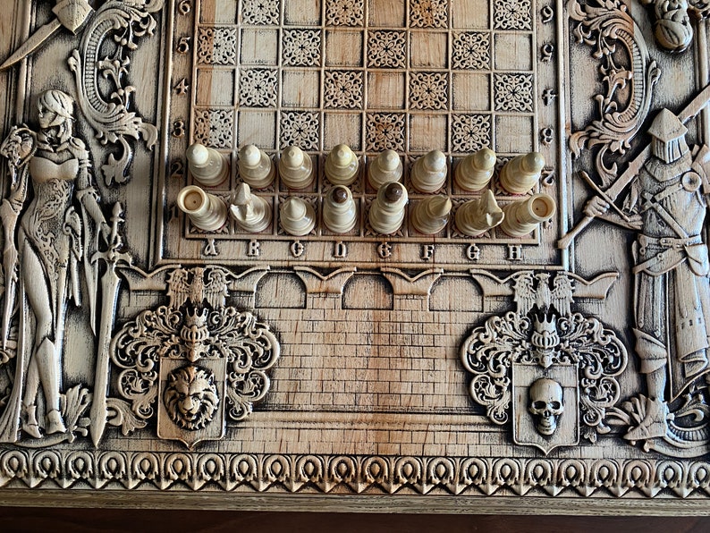 Op de afbeelding: Een houten schaakbord met ingewikkelde houtsnijwerk van ridders en andere figuren. Het bord is gemaakt van licht hout en heeft een donkere houten rand. De schaakstukken zijn wit en zijn op het bord in een beginpositie gerangschikt. Het bord heeft letters A tot en met H en nummers 1 tot en met 8 erop gedrukt.