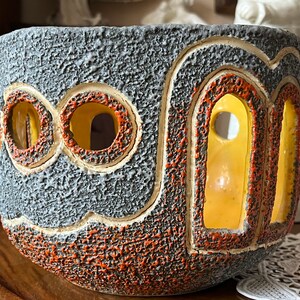 May include: A gray ceramic planter with orange and yellow accents. The planter has a textured surface and cut-out designs.