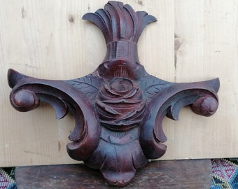 Op de afbeelding: Een donkerbruin houten gesneden ornament met een roosontwerp en een decoratieve bovenkant. Het ornament heeft een gedetailleerd, ingewikkeld ontwerp.