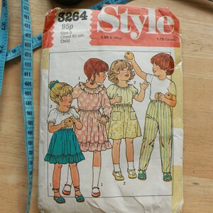May include: A vintage sewing pattern for children's clothing. The pattern is for a dress and trousers, and includes three different styles. The pattern is labelled "3264" and "Style".