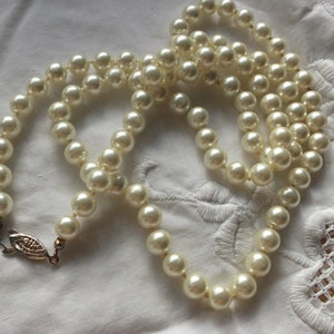 May include: A long strand of white faux pearl beads with a gold clasp.