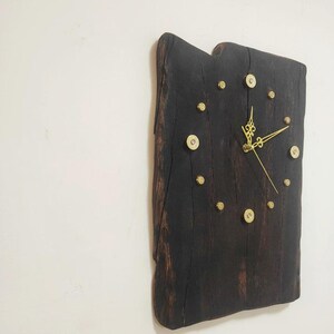 May include: A rustic, rectangular wall clock made from a dark brown, textured piece of wood. The clock features gold-colored hands and hour markers, and small, decorative gold accents. The clock is mounted on a white wall.