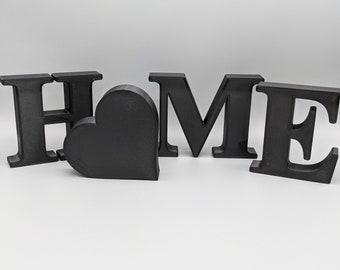 May include: Black wooden letters spelling "HOME" with a black heart in between the "H" and "O".