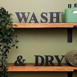 May include: Two wooden shelves with black metal brackets. The top shelf has the word "WASH" in black block letters. The bottom shelf has the word "& DRY" in black block letters.