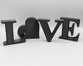 May include: Black wooden letters spelling out the word "LOVE" with a black heart in the middle.