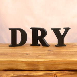 May include: Black wooden letters spelling out the word "DRY" on a wooden surface.